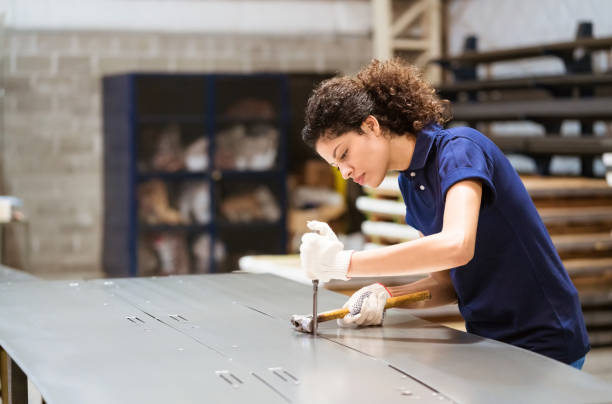 Serious female engineer hammering metallic sheet Serious female apprentice hammering on metal sheet. Mid adult engineer is working in industry. She is wearing uniform. sheet metal stock pictures, royalty-free photos & images