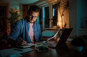 istock Serious handsome man working late from his home office 1340712779