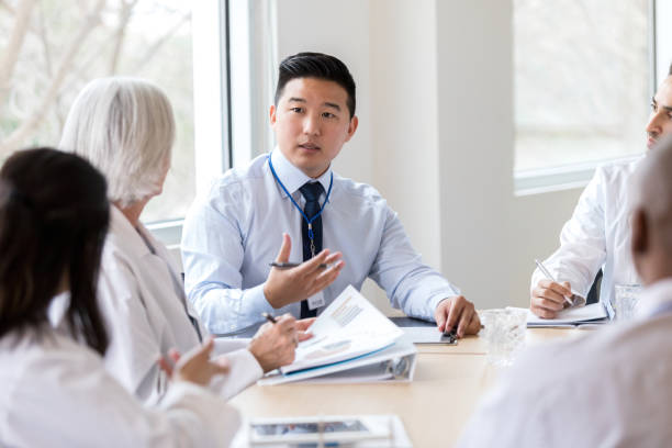 Serious hospital executive talks during meeting Male hospital administrator gestures while discussing a serious topic during a staff meeting. administrator stock pictures, royalty-free photos & images