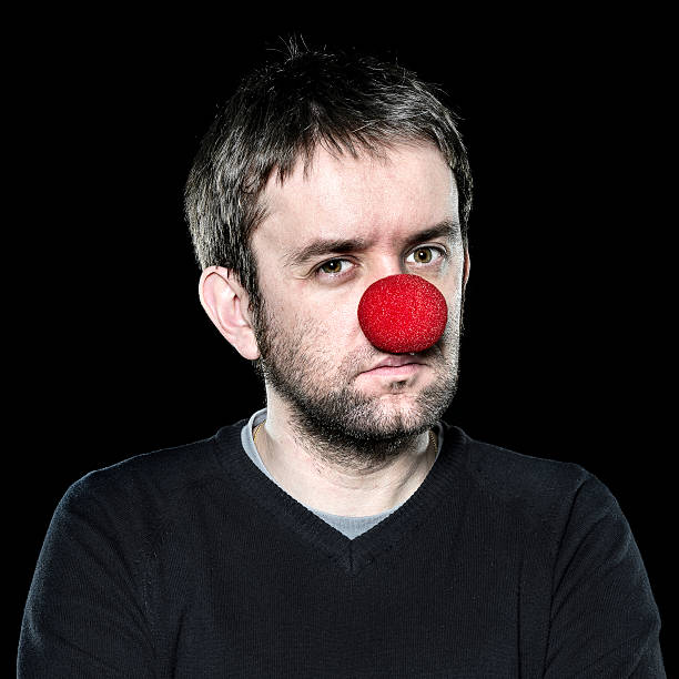 Serious man with red nose on black background Serious man with red nose on black background clown's nose stock pictures, royalty-free photos & images