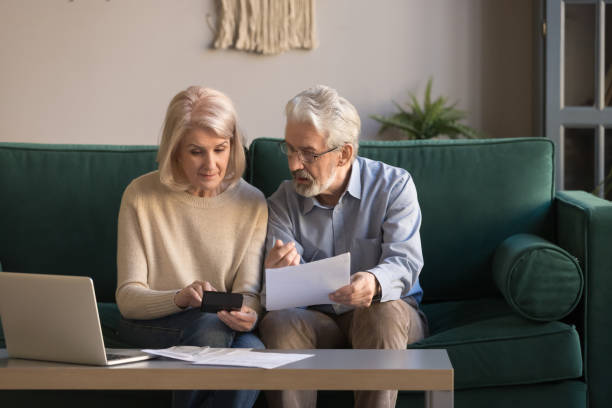 couples matures sérieux calculant des factures, vérifiant les finances intérieures - retraite photos et images de collection