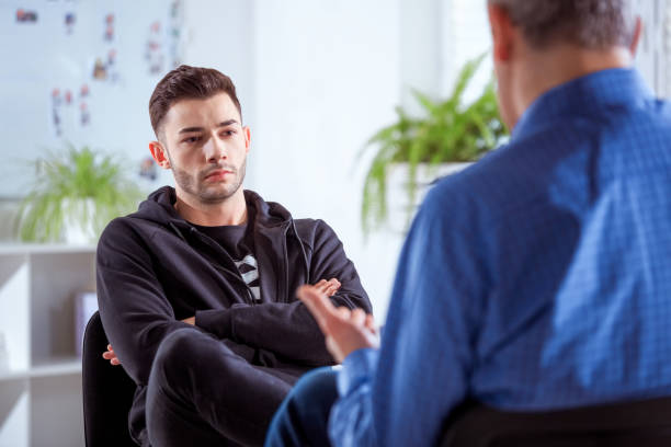 Serious university student listening to therapist Serious student listening to therapist. Mature professional advising young man during session. They are sitting in meeting at lecture hall. psychotherapy stock pictures, royalty-free photos & images