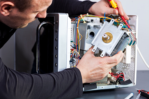 Serviceman Electrician Repairs A Magnetron In The Microwave Stock Photo