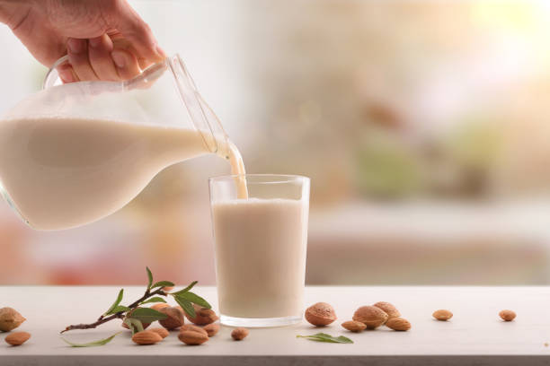 Que sirve el vaso de leche de almendras en mesa blanca en cocina - foto de stock