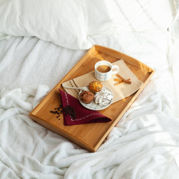 Serving tray with sweet dessert and cup of coffee in bed, white sheets, and blanket in the hotel. stock photo