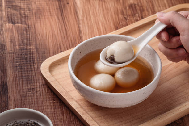 Sesame big tangyuan with syrup soup. Close up of sesame big tangyuan (tang yuan, glutinous rice dumpling balls) with sweet syrup soup in a bowl on wooden table background for Winter solstice festival food. chinese lantern festival stock pictures, royalty-free photos & images