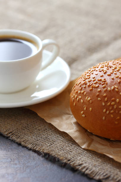 A sesame bun and a mug of coffee on kraft paper and burlap tablecloth. A sesame bun and a mug of coffee on kraft paper and burlap tablecloth. burger wrapped in paper stock pictures, royalty-free photos & images
