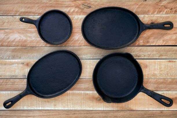 Set of four round and oval cast iron skillets of different sizes on a wooden background. stock photo