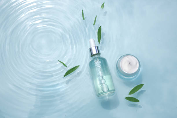 Set of moisturizing cosmetic products on water with drops. Glass bottle with pipette, serum, collagen and jar of cream on aqua surface with waves stock photo