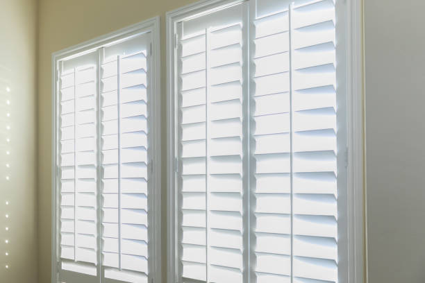 A set of open white plantation shutters in a light butter yelllow room stock photo