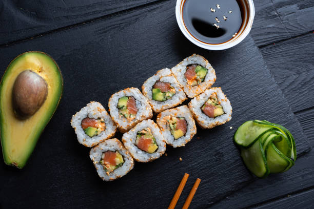 Set of sushi rolls with cream cheese, rice and salmon on a black board decorated with soy sauce and avocado on a dark wooden background. Japanese cuisine. Food photo background stock photo