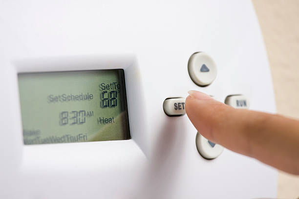 Setting electronic thermostat heat to 68 degrees Female hand setting thermostat to 68 degrees Fahrenheit to save energy in the winter. fahrenheit stock pictures, royalty-free photos & images