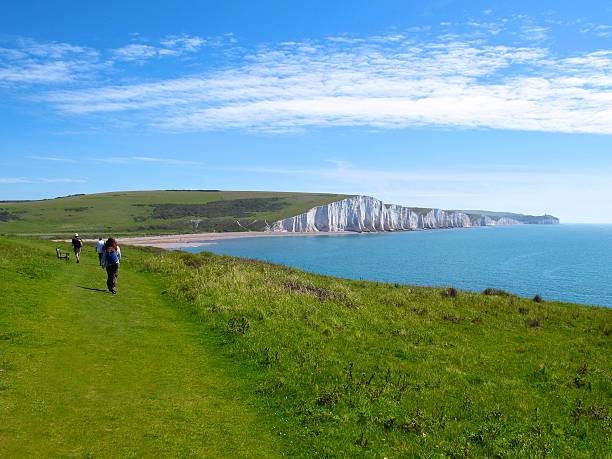 Seven Sisters England distant hikers on grassy path white cliffs stock photo