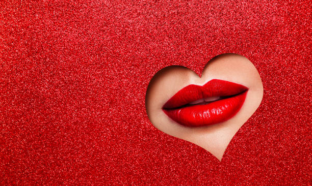 Sexy Red Lips Makeup Close up. Beauty Red Lipstick Make up look out Heart Hole Glitter Red Color Paper Background Copy Space. Cosmetic Salon Professional Advertising stock photo
