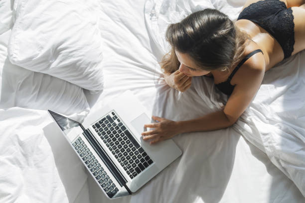 性感的女人在黑色內衣躺在床上, 並使用筆記本電腦 - online sex 個照片及圖片檔