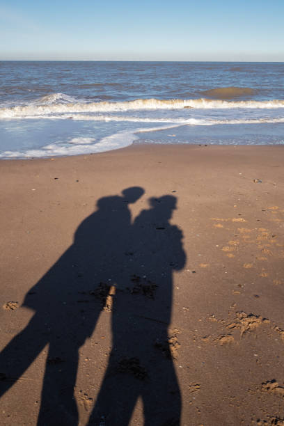 Shadow of a couple walking along the beach in winter stock photo