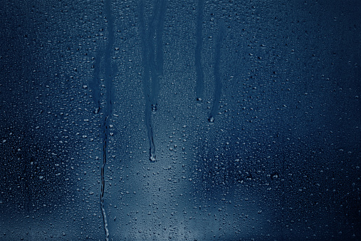 Water runs down a dark window covered in condensation