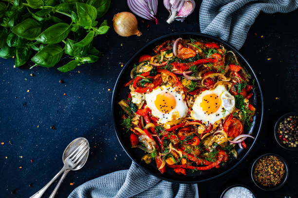 Shakshouka - fried eggs with vegetables on black wooden table stock photo