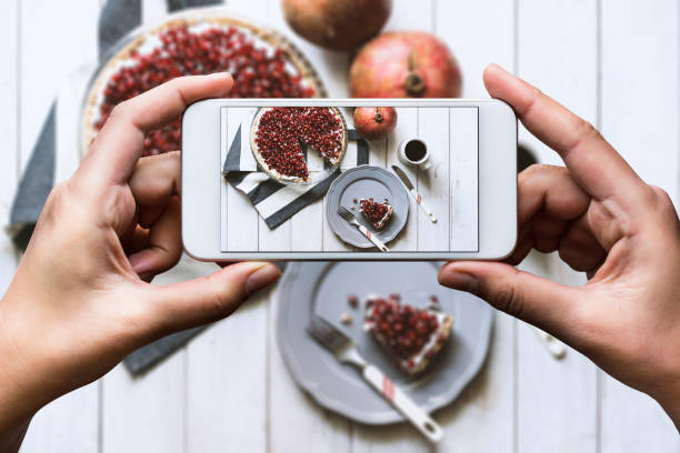 Share the moment Hand taking top view shot of table. Homemade tart, topped with fresh pomegranate and cup of coffee are on the table. baking photos stock pictures, royalty-free photos & images
