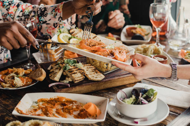 Sharing is Caring Point of view image of a group of multi-ethnic friends sharing multiple dishes, with a plate of prawns as the main focus. seafood stock pictures, royalty-free photos & images