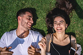 Couple lying down on a grass area in a park while listening to music together