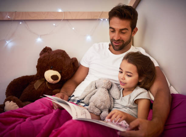 She can't sleep without Dad first reading her a story Cropped shot of a father reading a book with his little daughter in bed at home bed time story books for kids stock pictures, royalty-free photos & images