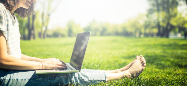 Young woman relaxed barefoot in park is working or studying on laptop