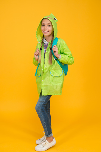 She is cool. Happy small child wear fashion rain jacket on yellow background. Small child smiling with autumn look. Small girl ready for rainy travel. Adorable small child smile in green raingear.