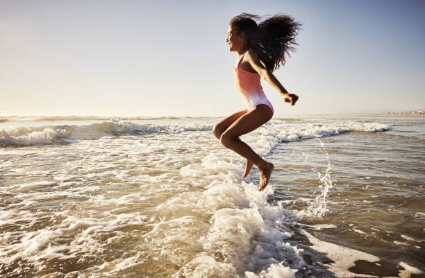 She loves jumping and skipping over all the waves Shot of a young girl having fun at the beach little girls in bathing suits stock pictures, royalty-free photos & images