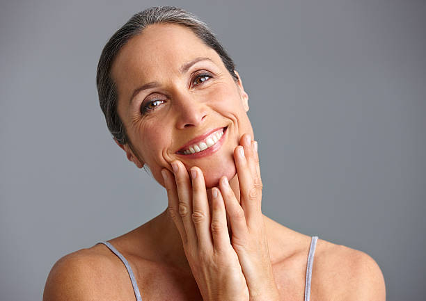 She takes good care of her skin Studio portrait of a beautiful mature woman posing against a gray background hand on chin stock pictures, royalty-free photos & images