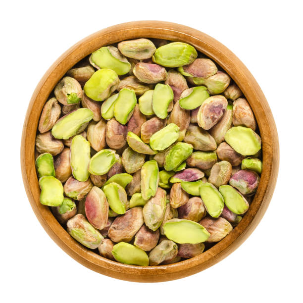 Shelled pistachio kernels in wooden bowl over white Shelled pistachio kernels in wooden bowl. Dried seeds and ripe fruits of Pistacia vera. Snack. Isolated macro food photo close up from above on white background. pistachio stock pictures, royalty-free photos & images