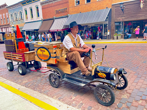 Deadwood, South Dakota, USA - July 7, 2022: A “Sheriff” drives a miniature antique car replica pulling a trailer of safety cones and other equipment following the daily re-enactment of a gunslinger “shoot-out” on historic Main Street.