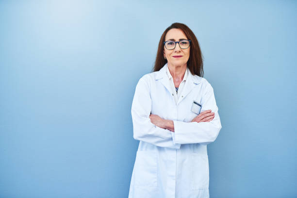 She's been a leading expert in the field Studio portrait of a mature scientist standing against a blue background lab coat stock pictures, royalty-free photos & images