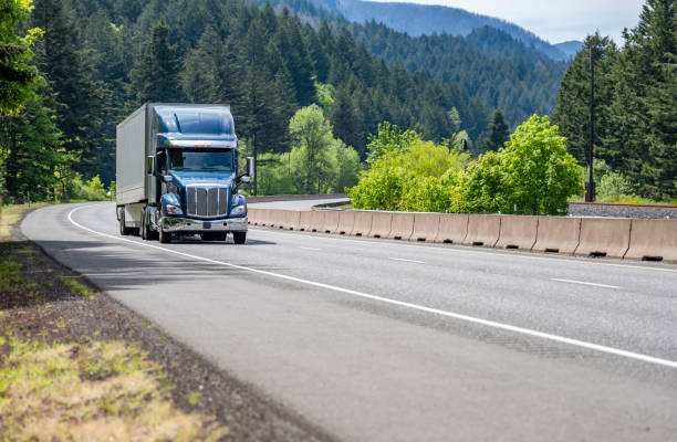 Shiny blue big rig semi truck transporting cargo in dry van semi trailer running on the winding road in Columbia Gorge stock photo