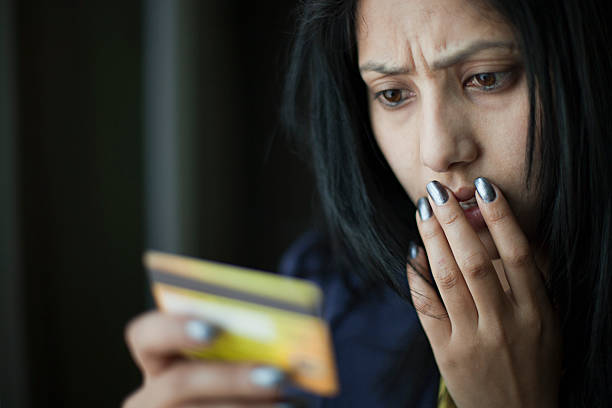 shocked and worried young woman looking at credit card. - geldstress stockfoto's en -beelden