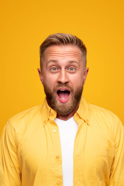 Shocked bearded man with mouth opened Happy stunned bearded male in casual yellow shirt looking at camera with disbelief while getting unbelievable shocking news on yellow background mouth open stock pictures, royalty-free photos & images