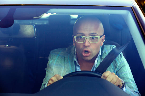 Shocked man driving car having accident Shot through windscreen of car of man in glasses driving and having accident looking extremely shocked holding steering wheel and looking away. worried man funny stock pictures, royalty-free photos & images