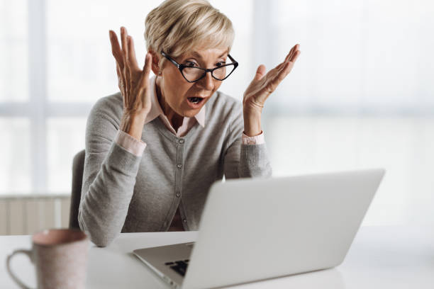 Shocked senior woman working on laptop in the office stock photo