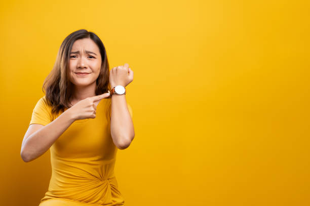 Shocked woman holding hand with wrist watch isolated on a yellow background stock photo