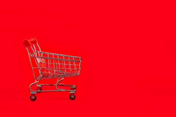 Shopaholic shopper concept.Close up view of one single shine tiny toy shopping cart on a bright red background. Sale, discount stock photo