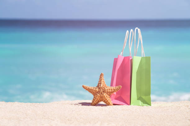 Shopping bags and starfish on sand against turquoise caribbean sea water stock photo
