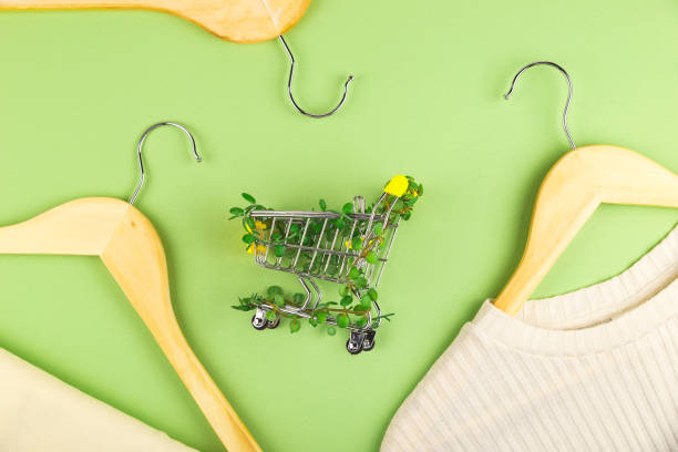 Shopping cart entwined with plants on green background among hangers. Sustainable eco lifestyle. Conscious consumption slow fashion Zero waste concept. Shopping cart entwined with plants on green background among hangers. Sustainable eco lifestyle. Top view flat lay slow fashion stock pictures, royalty-free photos & images