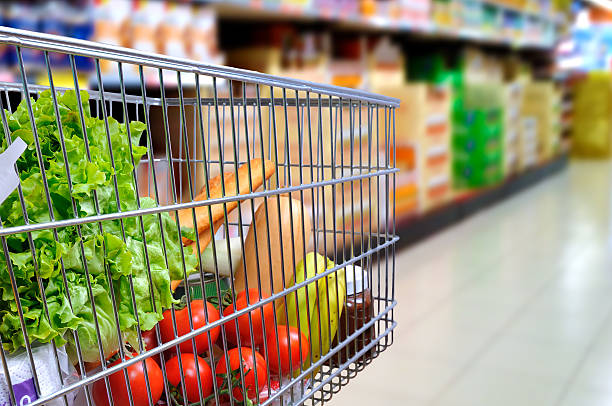 Shopping cart full of food in supermarket aisle side tilt stock photo