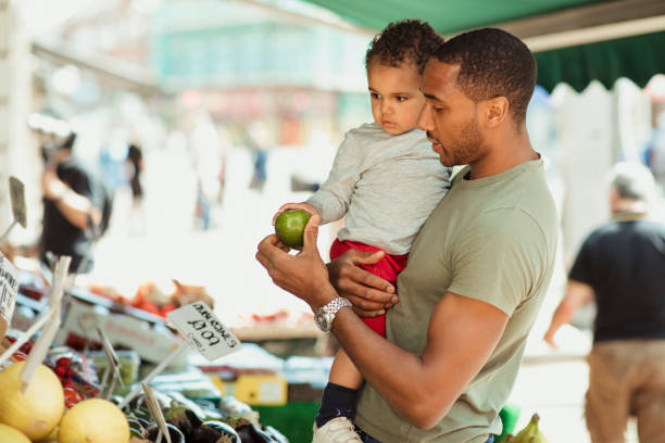 Shopping with a Healthy Lifestyle Father holding his son while they are out shopping, looking at different fruits. farmer's market stock pictures, royalty-free photos & images