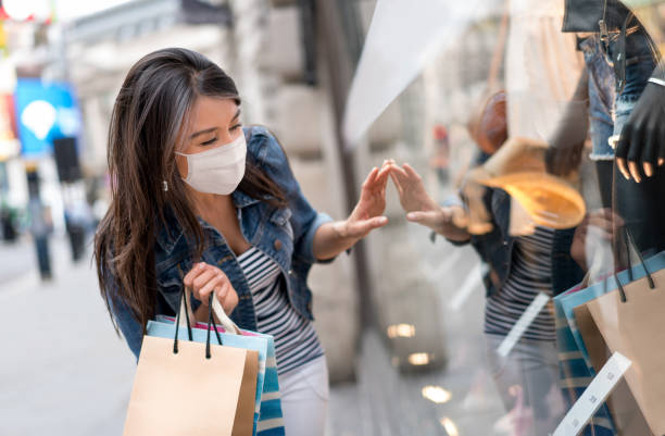 winkelende vrouw die een facemask tijdens pandemie draagt en een venster bekijkt - etalages kijken stockfoto's en -beelden