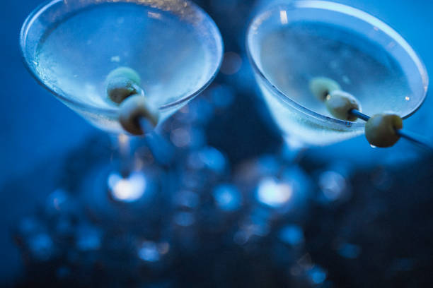 Shot at night in Nassau, in blue light, two dirty martinis with olives standing among ice cubes. Martini photography. dirty martini stock pictures, royalty-free photos & images