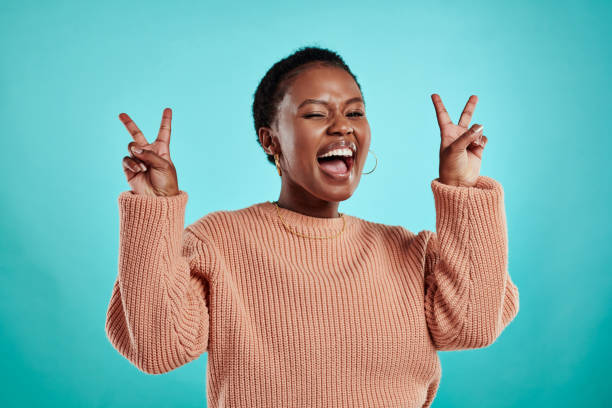 Shot of a beautiful young woman showing the peace sign while standing against a turquoise background stock photo