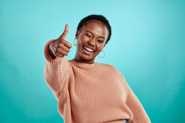 Shot of a beautiful young woman showing thumbs up while standing against a turquoise background stock photo
