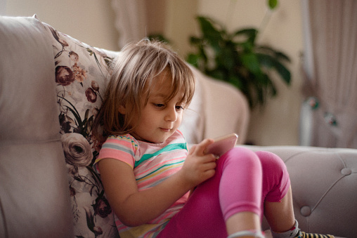 Shot of a cute little girl playing with a smart phone at home. Horizontal shot.