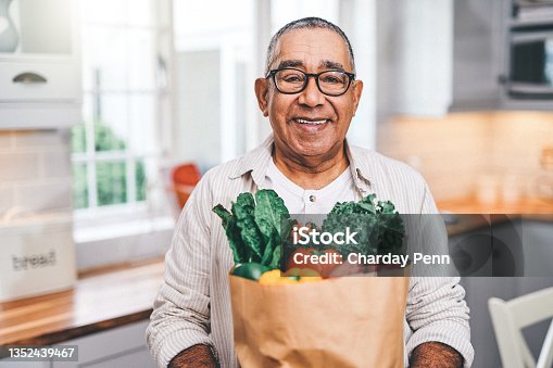 istock Shot of a elderly man holding a grocery bag in the kitchen 1352439467